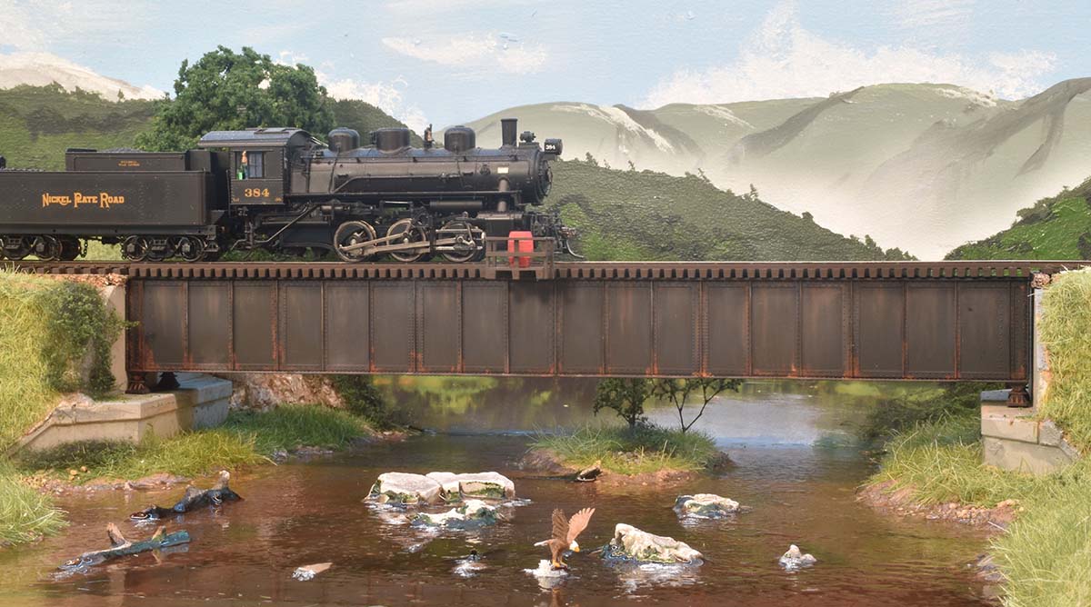 As #384 crosses Leaky Creek on the Wildcat Valley Railway, the engineer salutes the bald eagle’s fishing prowessin HO Scale by Dave Mashino, CID